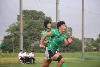 屋外のラグビーフィールドで、緑色のユニフォームを着た2人の選手が躍動する瞬間