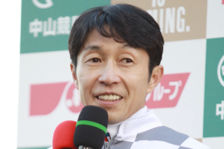 競馬場でマイクを手に笑顔を見せる騎手